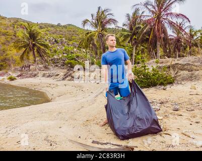 Homme en gants, ramasser les sacs en plastique qui polluent la mer. Problème de déchets de déchets déversés de déchets de déchets sur le sable de plage causé par la pollution artificielle et Banque D'Images