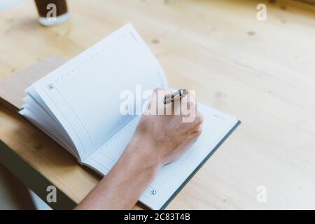 Jeune homme, personne méconnaissable écrivant des informations sur le bloc-notes, adolescent dans des vêtements décontractés planifie un horaire, quotidien, liste de tâches Banque D'Images
