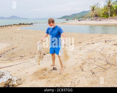 Homme en gants, ramasser les sacs en plastique qui polluent la mer. Problème de déchets de déchets déversés de déchets de déchets sur le sable de plage causé par la pollution artificielle et Banque D'Images