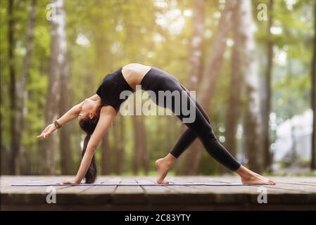 Gymnast fille est entraînement en train de faire l'exercice Bridge, asana Camatkarasana, Dancing Dog yoga pose. Sportif posant dans des vêtements noirs à l'extérieur Banque D'Images
