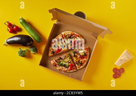 Savoureuse pizza italienne de salami et de légumes avec parmesan et ingrédients frais dans une boîte en carton à emporter ouverte sur fond jaune Banque D'Images