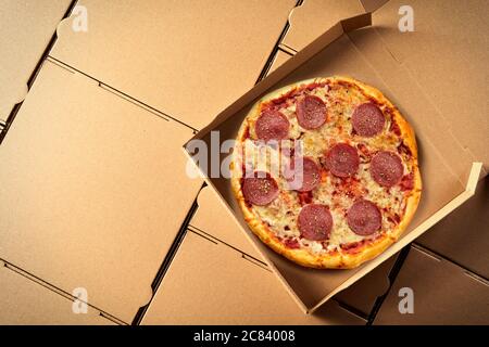 Pizza italienne traditionnelle salami dans une boîte à emporter en carton brun ouvert sur les boîtes génériques vierges supplémentaires dans une vue de dessus pour adver Banque D'Images