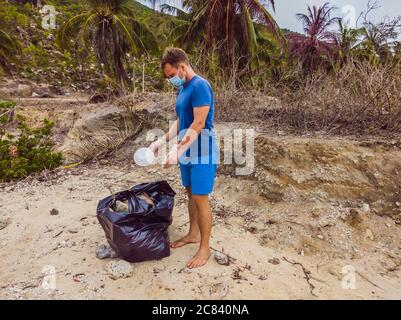 Homme en gants, ramasser les sacs en plastique qui polluent la mer. Problème de déchets de déchets déversés de déchets de déchets sur le sable de plage causé par la pollution artificielle et Banque D'Images