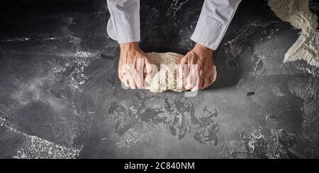 Cuisinez ou cuisinez la pâte pour les bases de pizza dans une pizzeria italienne en pétrissant la pâte avec ses mains sur un plateau fariné dans une bannière panoramique avec Banque D'Images