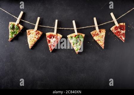 Portions de pizzas italiennes avec différentes garnitures accrocées à une ficelle formant une bordure supérieure sur l'ardoise avec l'espace d'imitation ci-dessous Banque D'Images