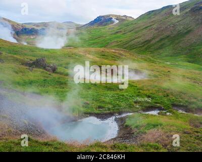 Vallée de Reykjavadalur avec sources d'eau chaude et piscine avec prairie d'herbe verte luxuriante et collines avec vapeur géothermique. Sud de l'Islande près de la ville de Hveragerdi Banque D'Images