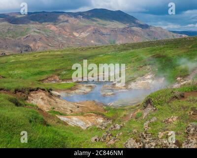 Vallée de Reykjavadalur avec sources d'eau chaude et piscine avec prairie d'herbe verte luxuriante et collines avec vapeur géothermique. Sud de l'Islande près de la ville de Hveragerdi Banque D'Images