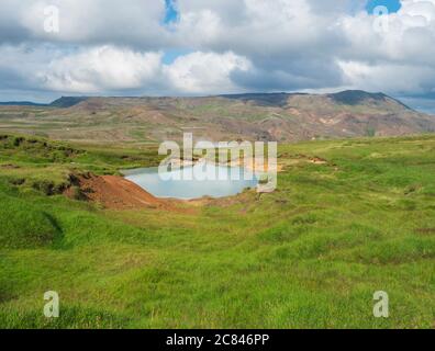 Vallée de Reykjavadalur avec sources d'eau chaude et piscine avec prairie d'herbe verte luxuriante et collines avec vapeur géothermique. Sud de l'Islande près de la ville de Hveragerdi Banque D'Images