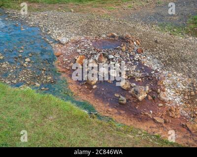 Fumarale d'eau bouillante rouge, orange et jaune coloré à la prairie d'herbe de la vallée de Reykjalur et à la vapeur géothermique. Sud de l'Islande près de Hveragerdi Banque D'Images