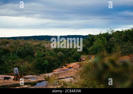 Vue de dessus d'une cascade d'eau calme à Cachoeira das Andorinhas à Ouro Preto entouré de verdure, de rochers rouges et d'un groupe de personnes pendant une après-midi nuageux Banque D'Images