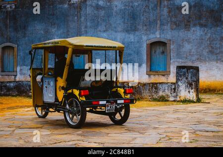 Un véhicule de tuk-tuk jaune de la compagnie Tuk Tour devant un mur de pierre d'une église touristique à Ouro Preto, Minas Gerais. Banque D'Images