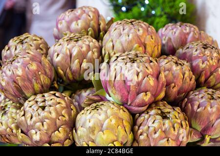 Grands artichauts Romanesco frais, têtes de fleurs vertes pourpres sur un marché. Banque D'Images