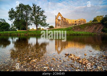 L'abbaye de Bolton brille pendant l'heure d'or, le matin d'été calme de juillet, la scène se reflète dans la rivière Wharfe qui coule doucement. Banque D'Images