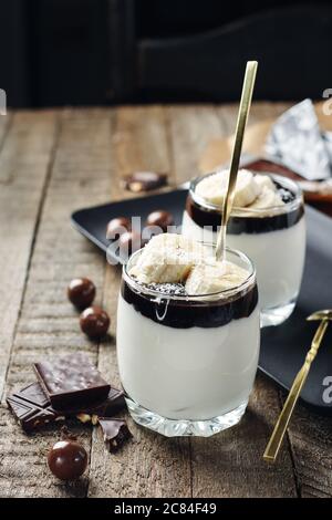 Dessert au lait avec crème à la banane et au chocolat dans un verre sur fond de bois. Banque D'Images