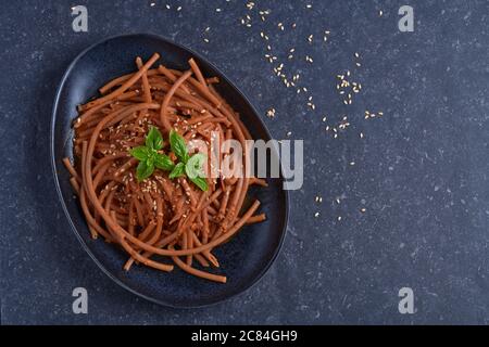 Bolognese vegan Bucatini, sans viande, avec sauce soja, tomates, graines de sésame et basilic frais, dans une assiette en pierre noire sur fond sombre. Banque D'Images