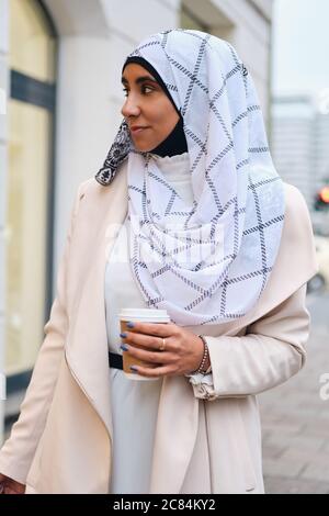 Jeune femme arabe attrayante dans hijab marchant dans la ville avec le café Banque D'Images