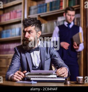 Portrait de l'écrivain élégant avec barbe. Homme portant un costume et un noeud papillon, assis près d'une machine à écrire rétro devant la bibliothèque ou l'intérieur vintage, défoqué Banque D'Images