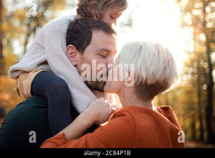 Jeune couple avec petite fille sur une promenade dans la forêt d'automne, embrassant. Banque D'Images