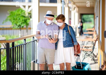 Couple senior avec masques et bagages à l'extérieur de l'appartement en vacances. Banque D'Images