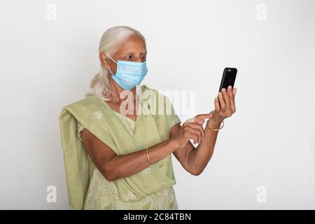 Femme indienne mature portant un masque de protection Covid, grand-mère indienne vérifie son téléphone portable Banque D'Images