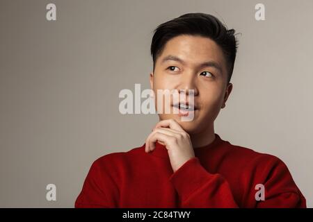 Image d'un homme asiatique charmant posant et regardant de côté isolé sur fond gris Banque D'Images