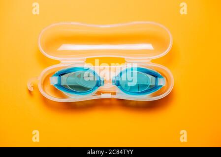 Lunettes de natation bleues, avec sangle en caoutchouc dans le boîtier en plastique, sur fond jaune. Personne, concept de produit Banque D'Images