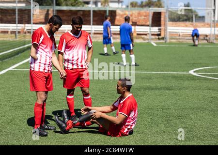 Deux équipes multiethniques de hommes de cinq joueurs de football de côté portant une bande d'équipe jouant un jeu sur un terrain de sport au soleil, joueur avec prothétique l Banque D'Images