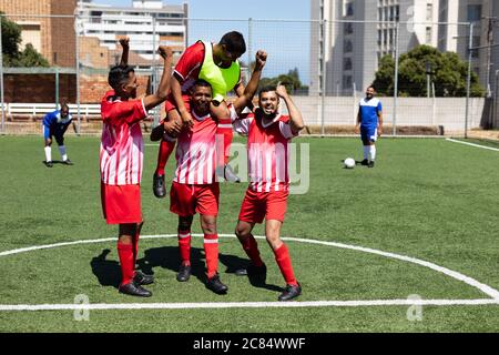 Deux équipes multiethniques de joueurs de football masculin de cinq a côté portant une bande d'équipe jouant un match sur un terrain de sport au soleil, célébrant Victory carr Banque D'Images