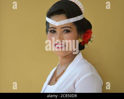 La femme indonésienne balinaise porte une tenue blanche et sourit pour la caméra lors d'une cérémonie religieuse du temple hindou (festival Odalan). Banque D'Images