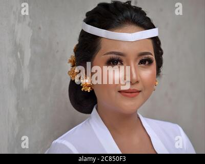 Belle femme indonésienne balinaise porte une tenue blanche et pose pour la caméra lors d'une cérémonie religieuse de temple hindou (festival Odalan). Banque D'Images