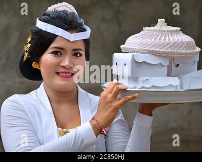 La femme indonésienne balinaise porte un plateau avec des collations lors d'une cérémonie religieuse de temple hindou (festival Odalan) et sourit pour la caméra. Banque D'Images