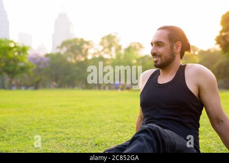 Joyeux jeune homme indien beau barbu pensant et assis au parc Banque D'Images