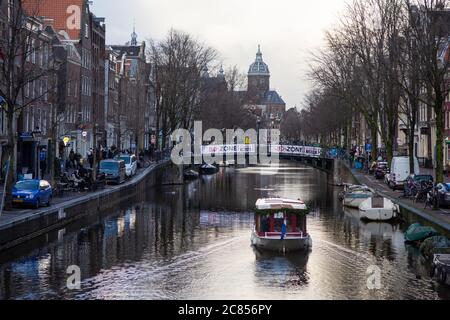 Amsterdam, pays-Bas - janvier 15 2019: Un bateau voyage le long d'un canal dans le centre du quartier rouge de Wallen d'Amsterdam. Banque D'Images