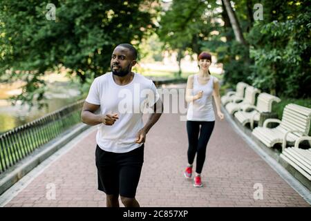 Sport fitness couple, jeune homme africain et femme caucasienne jogging en plein air dans la nature, sur la route du parc de la ville. Deux coureurs s'entraîner ensemble. Concentrez-vous sur le Banque D'Images