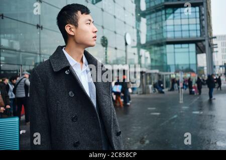 Vue latérale de jeunes hommes d'affaires asiatiques regardant en toute confiance en attendant le taxi près de l'aéroport Banque D'Images