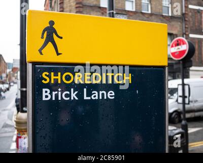 Un panneau de signalisation sur une rue animée de Londres indique aux piétons qu'ils sont à Shoreditch, sur Brick Lane. Banque D'Images