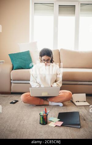 Photo vue de face d'une femme caucasienne avec lunettes faisant des devoirs sur le sol à l'aide d'un ordinateur portable et de dossiers Banque D'Images