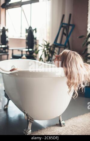 Femme caucasienne âgée avec cheveux blonds se relaxant dans une baignoire à la maison tout en mettant sur le visage une crème anti-âge Banque D'Images