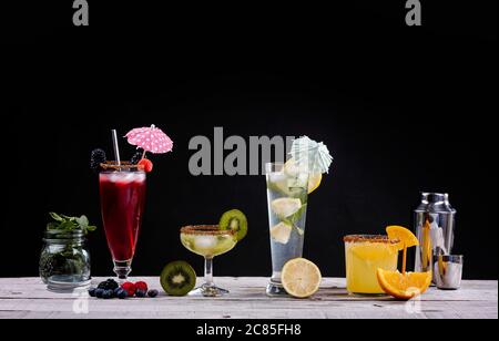 cocktails de différents fruits dans des verres en cristal sur un panneau en bois et un fond noir Banque D'Images