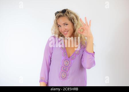 Jolie femme blonde dans un caftan lilas souriant et faisant un geste correct Banque D'Images