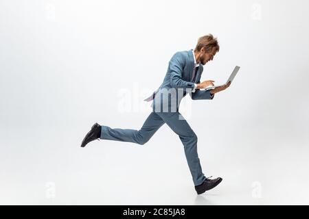 Saisie. Homme dans des vêtements de bureau courant, jogging sur fond blanc comme un athlète professionnel, sportif. Un look inhabituel pour un homme d'affaires en mouvement, une action avec une balle. Sport, mode de vie sain, créativité. Banque D'Images