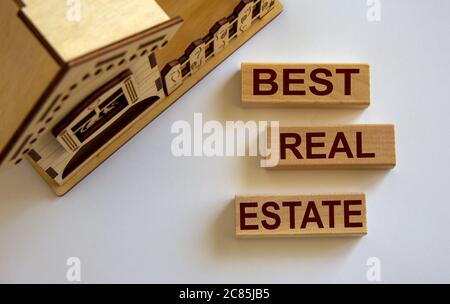 Les blocs en bois forment les mots « meilleur immobilier » près de la maison miniature. Fond blanc. Banque D'Images