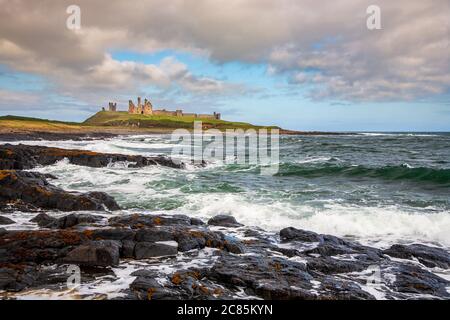 Vagues se brisant sur les roches ignées noires du château de Dunstanburgh, Northumberland, Angleterre Banque D'Images