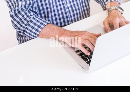 Homme senior en chemise à carreaux, tapant sur un ordinateur portable gris. Concept de télétravail. Banque D'Images