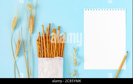 Bâtonnets salés dans un sac en papier écologique blanc avec épis de blé sur fond bleu Banque D'Images