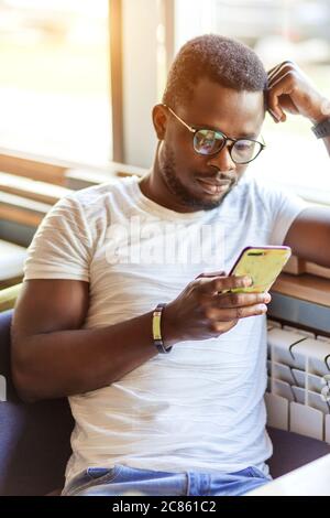 Un gars afro-américain pensif lisant le message dans un smartphone dans une pizzeria partageant la pizza avec les meilleurs amis, souriant un gars noir attrayant ayant le talkin amusant Banque D'Images