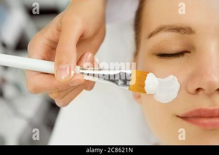 Gros plan d'une esthéticienne appliquant un masque facial sur une jeune femme visage service client traitement thérapie thérapeute dermatologie cosmétologie refres Banque D'Images