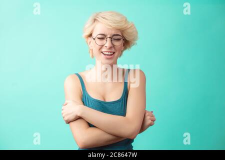 Belle blonde souriante femme avec coupe de cheveux portant bleu haut regardant l'appareil photo se embrassant. Isolé sur fond bleu. Banque D'Images