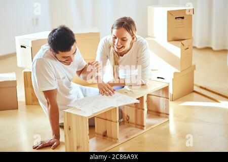 Le couple lit les instructions pour l'assemblage de meubles dans une nouvelle maison avec des boîtes mobiles sur l'arrière-plan Banque D'Images