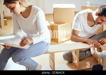 Le couple lit les instructions pour l'assemblage de meubles dans une nouvelle maison avec des boîtes mobiles sur l'arrière-plan Banque D'Images